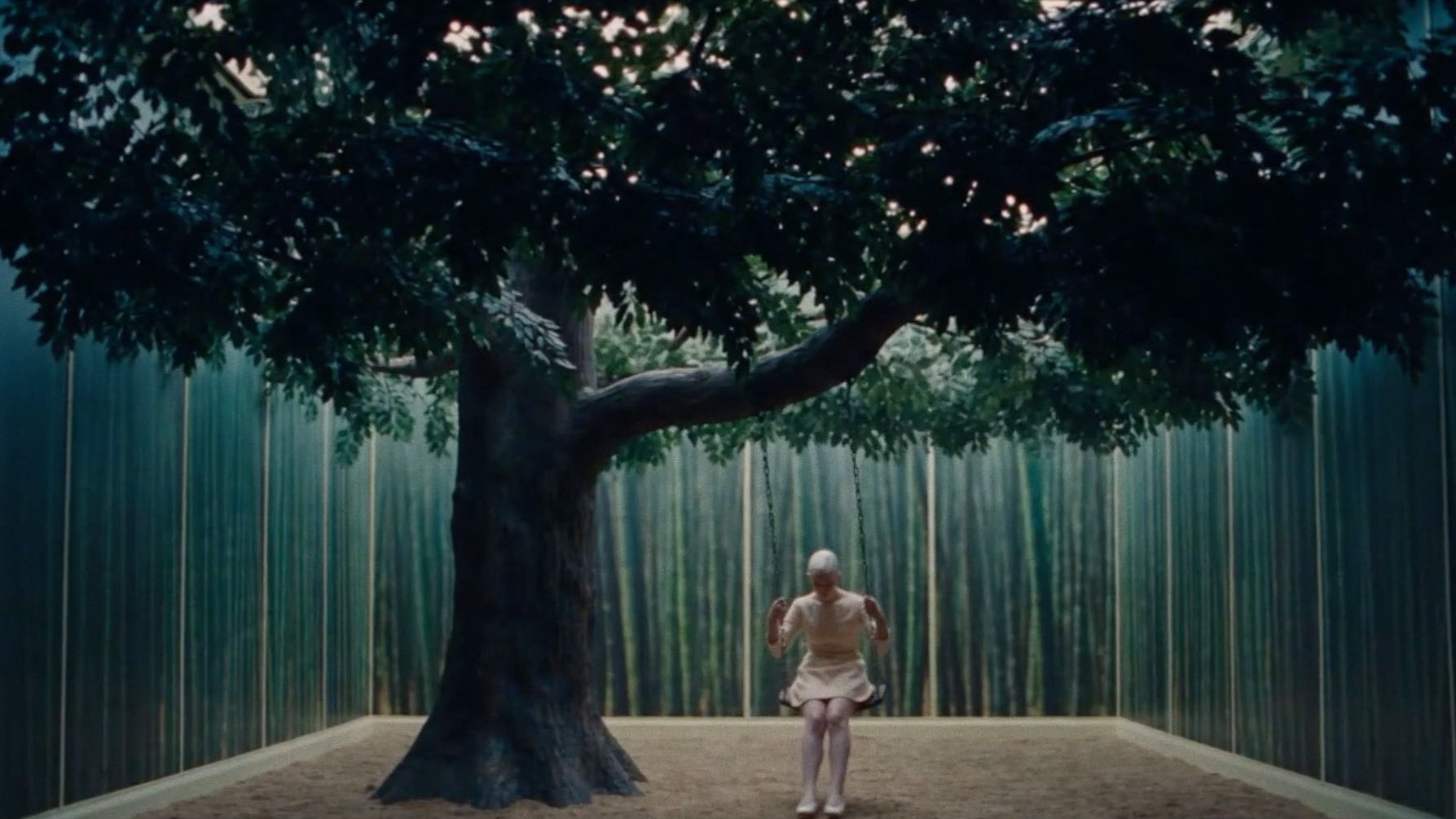 A figure on a swing beneath a single tree, inside a walled set of painted bamboo